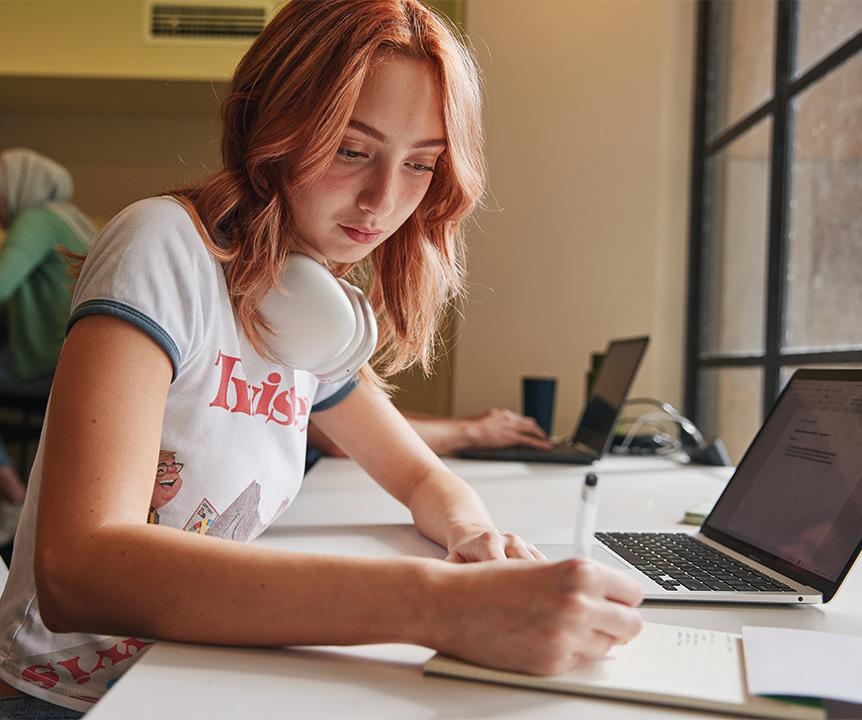A student is sitting at a desk writing in her notebook.