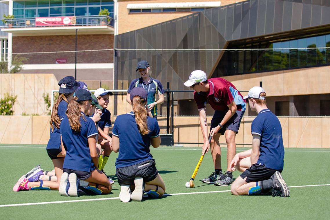 PE teacher demonstrating how to play hockey to high school students