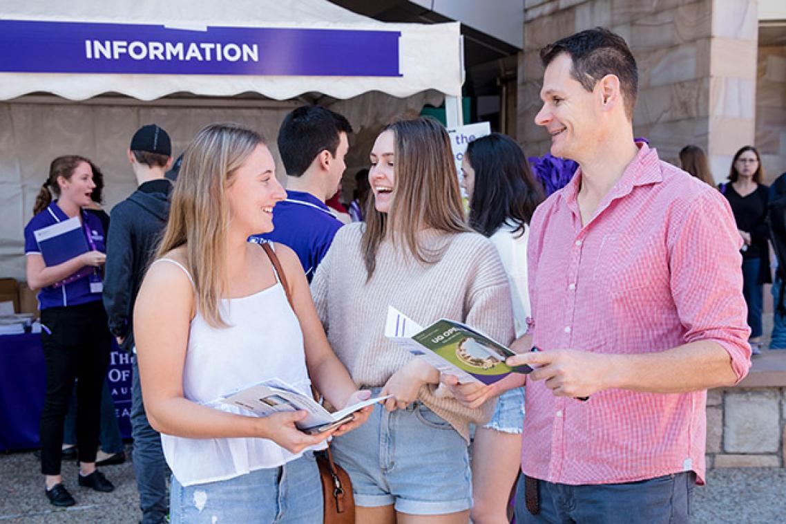 A father stands outside the information tent at UQ Open Day with his two daughters, looking at a program and chatting