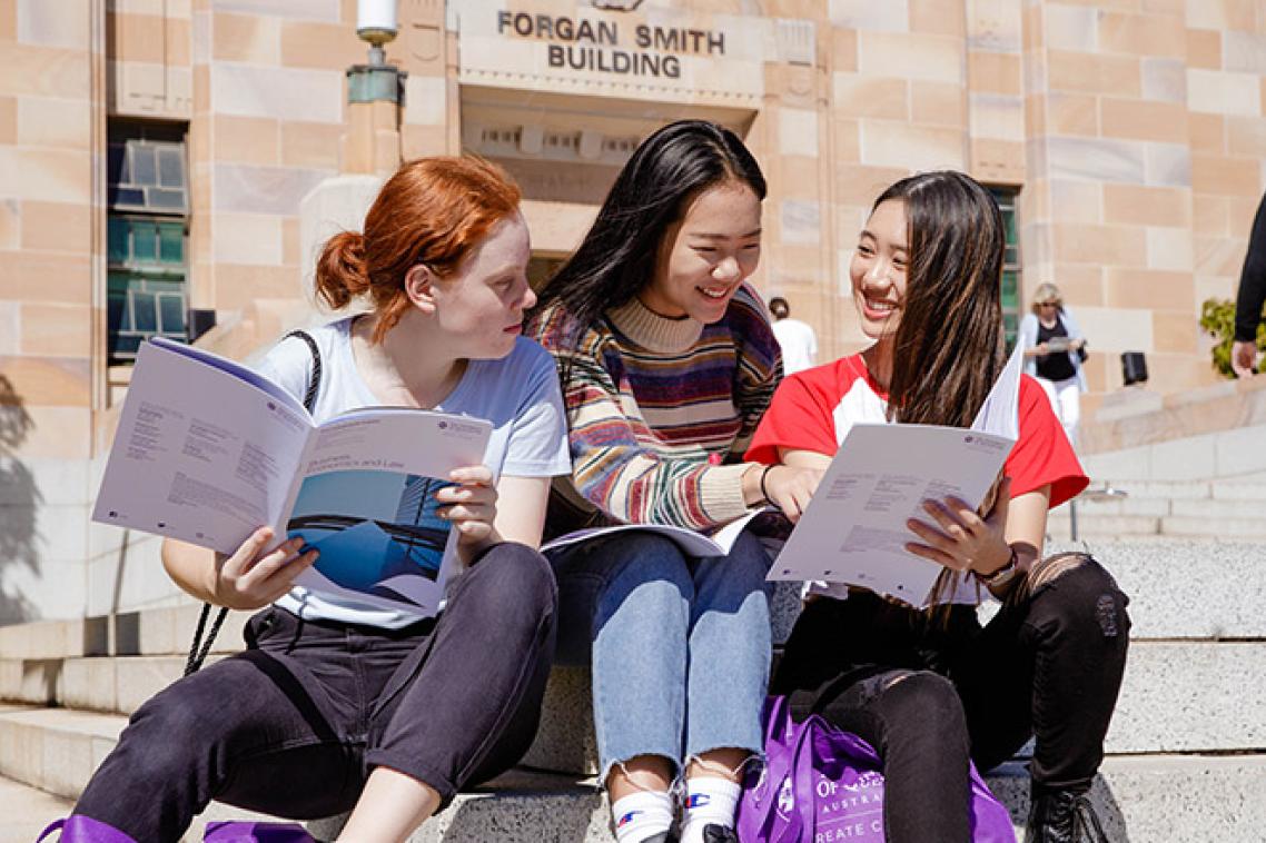 Three young women browse brochures outside UQ's sandstone buildings on Open Day