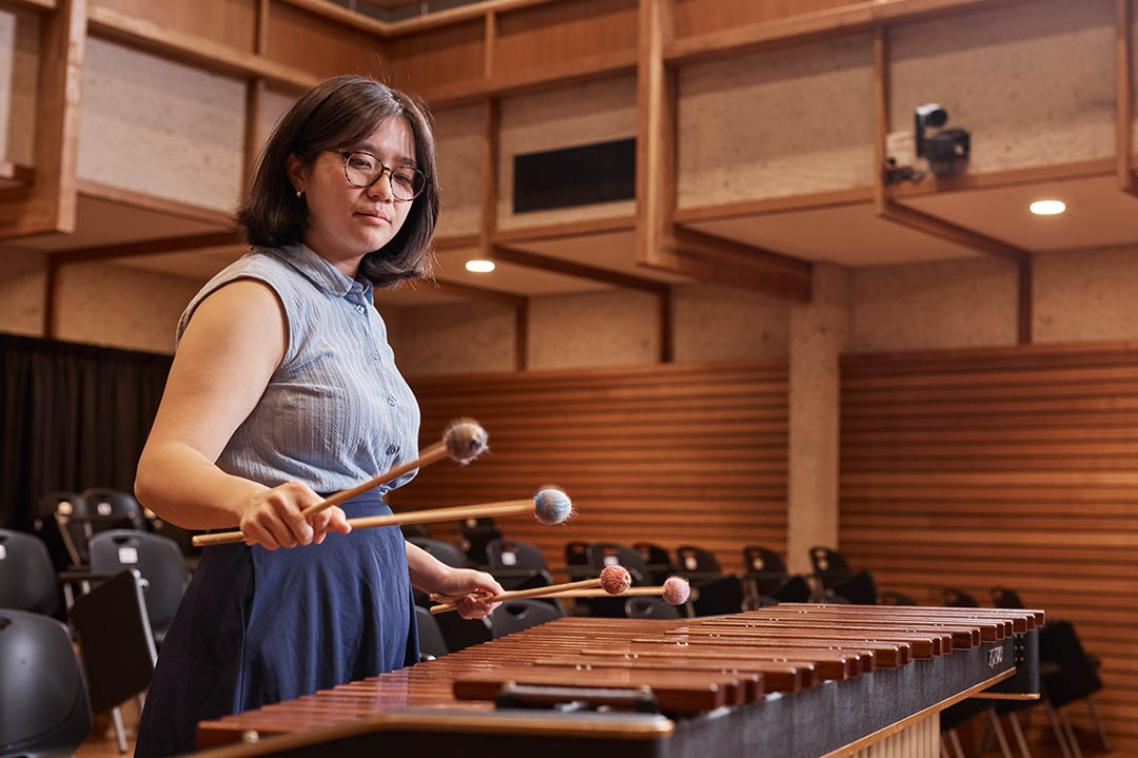 A woman plays a xylophone in a wood panelled room