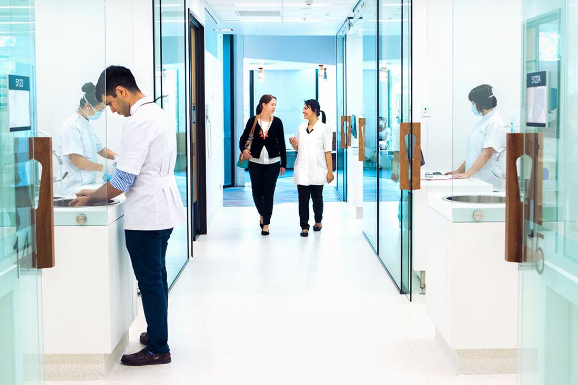 Two women walking along the glass walled corridor of a modern medical facility