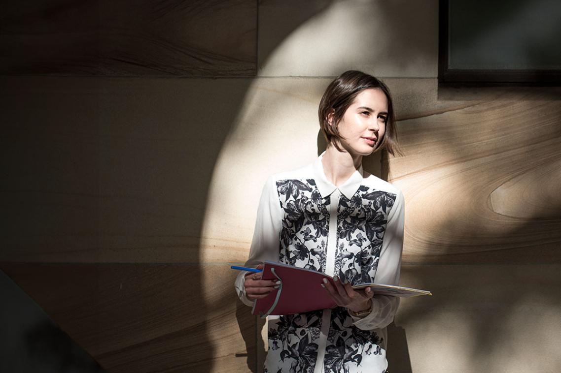 Student leaning on sandstone wall looking to right off-screen