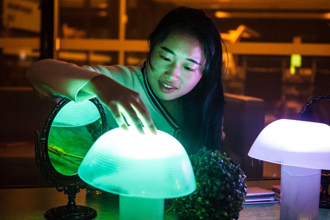Student in dimly lit room touches a glowing lamp. 