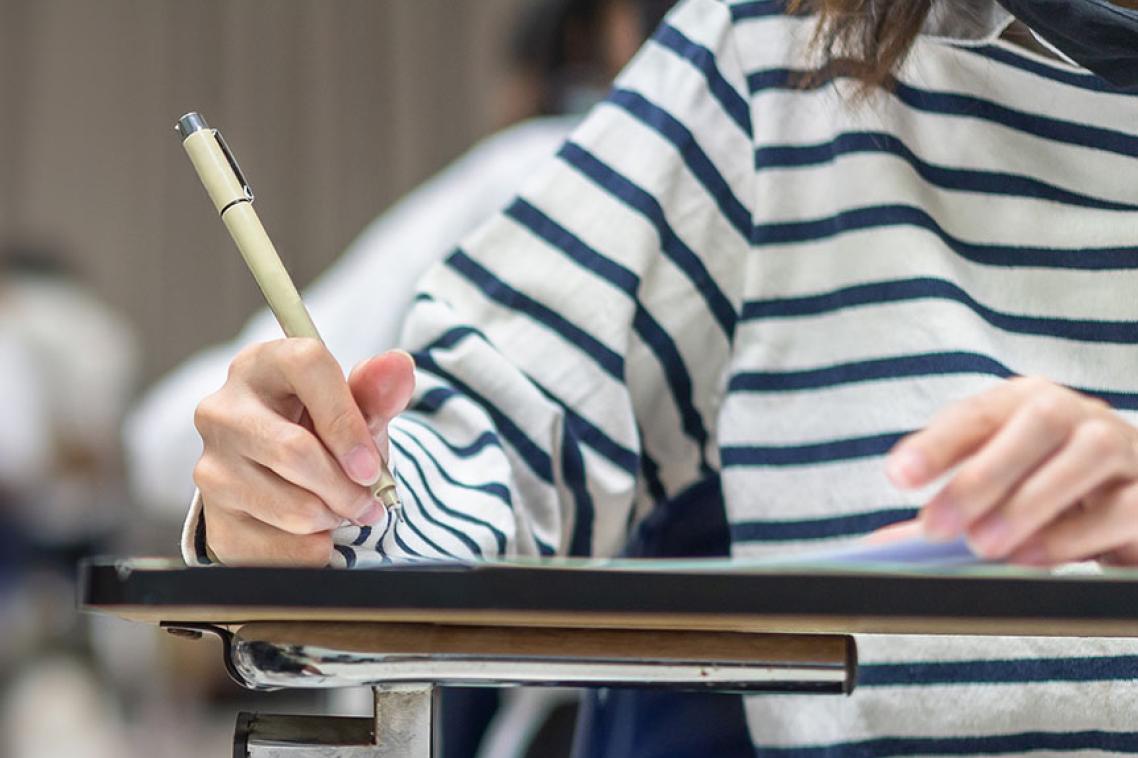 Student in striped shirt in classroom writing notes.