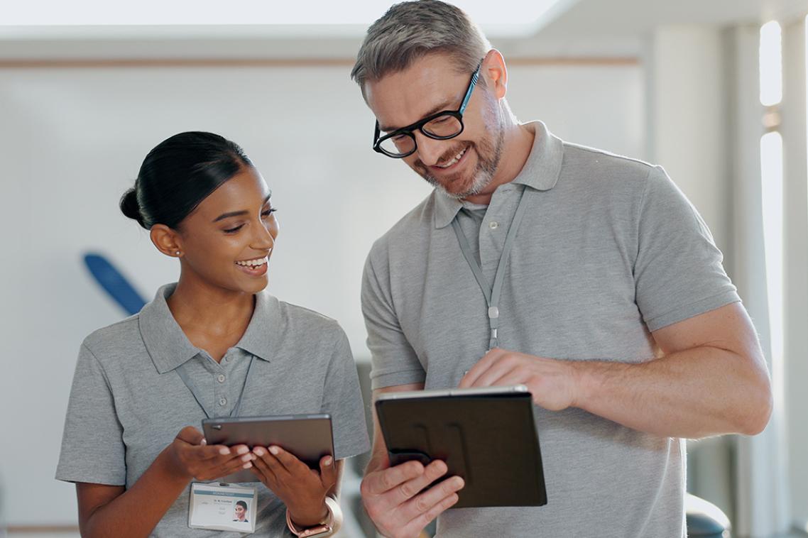 Two people in grey polo shirts discuss data on tablets in a clinical setting