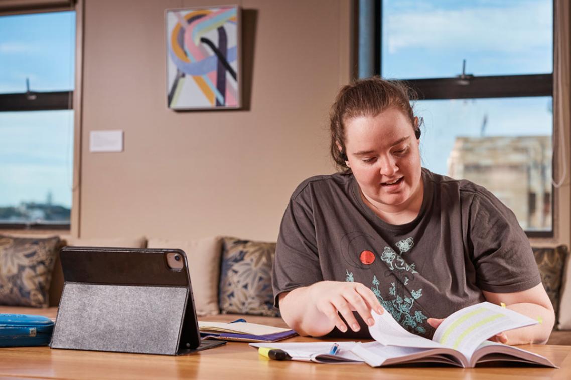 A UQ student highlights text in a textbook with an ipad open beside them