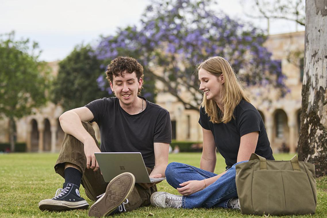 2 students sitting on the grass in the Great Court looking at a laptop.
